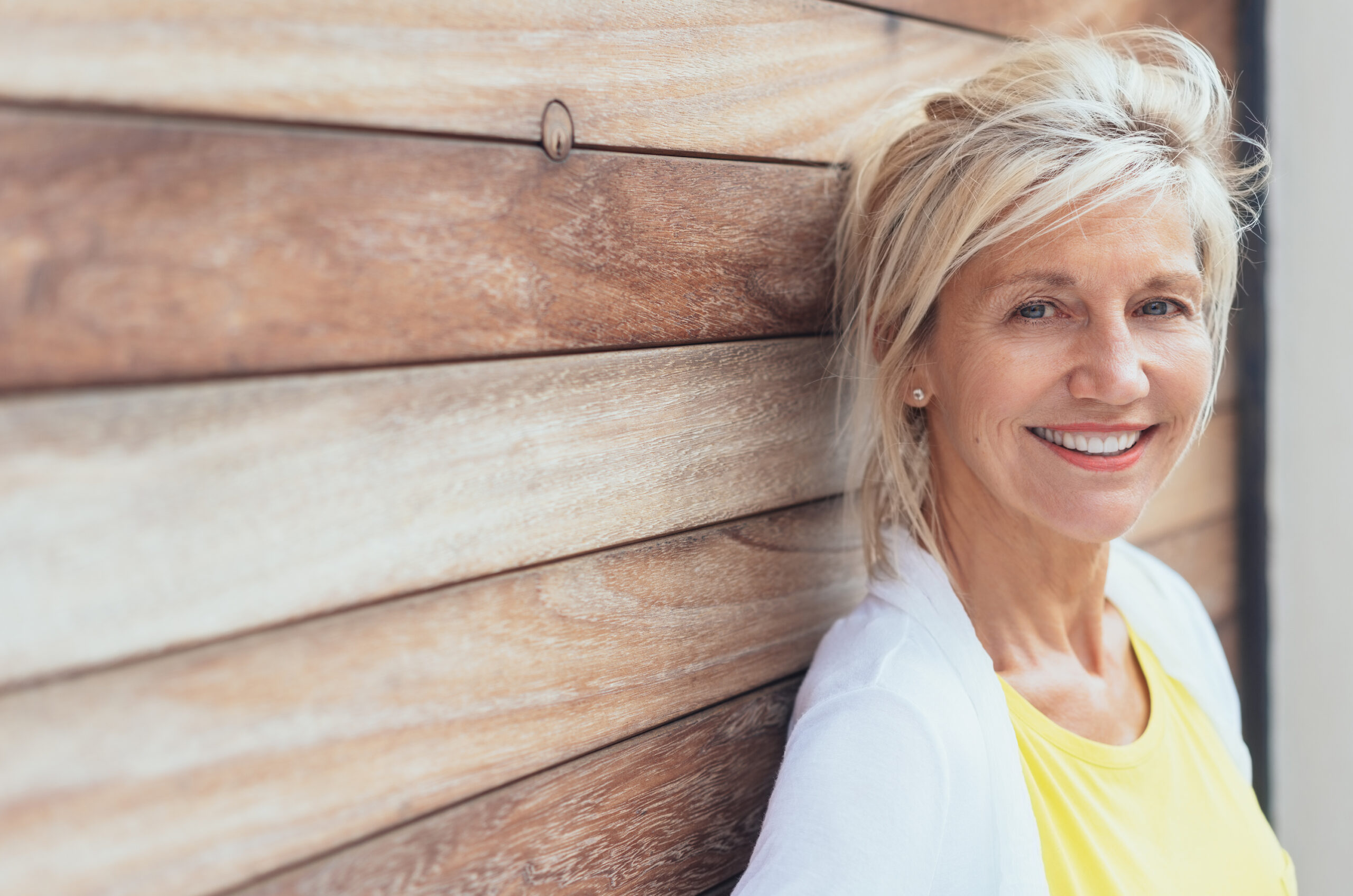 Smiling blond woman leaning on a wooden wall with natural timber boards