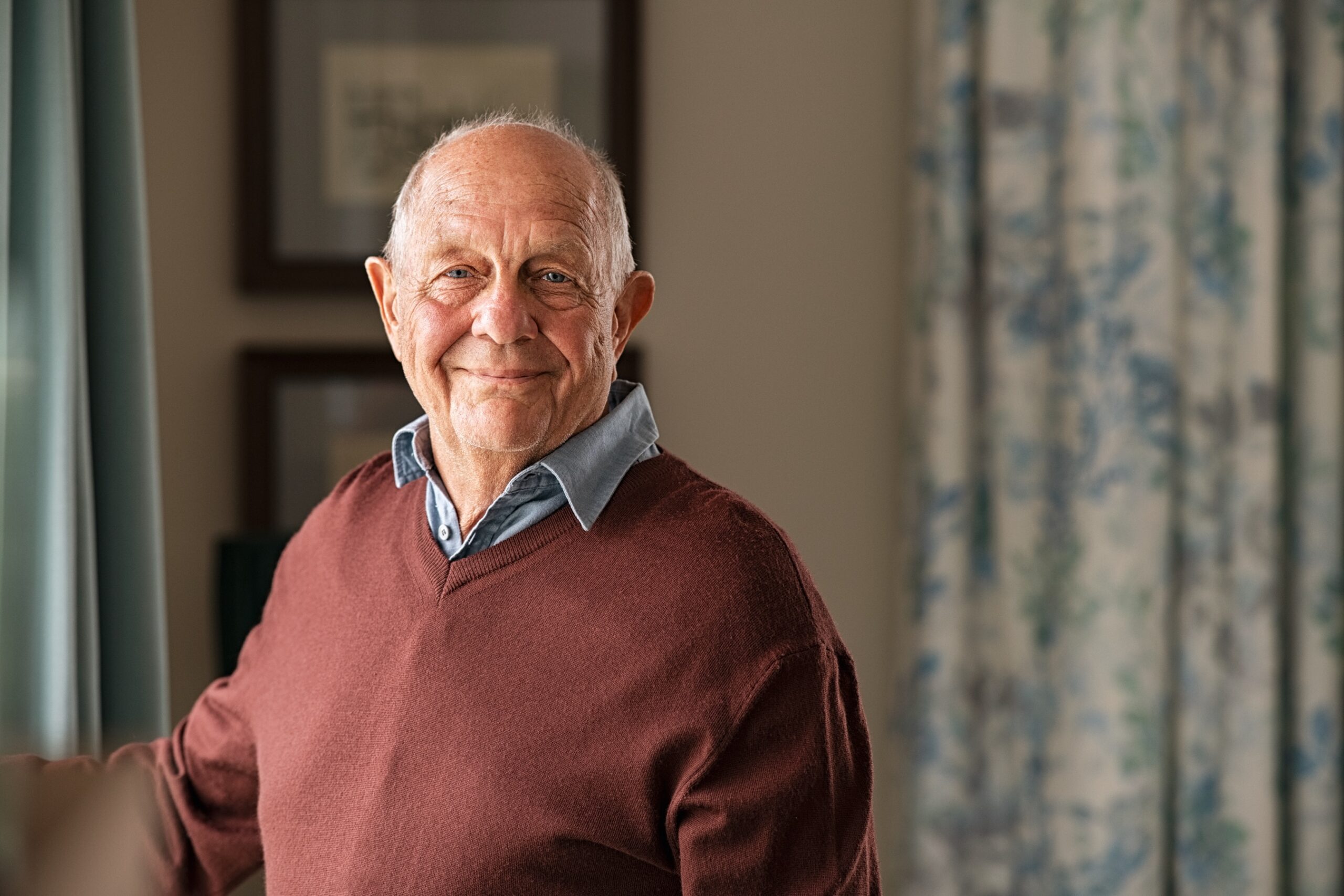 Portrait of happy retired senior man standing at home near window.