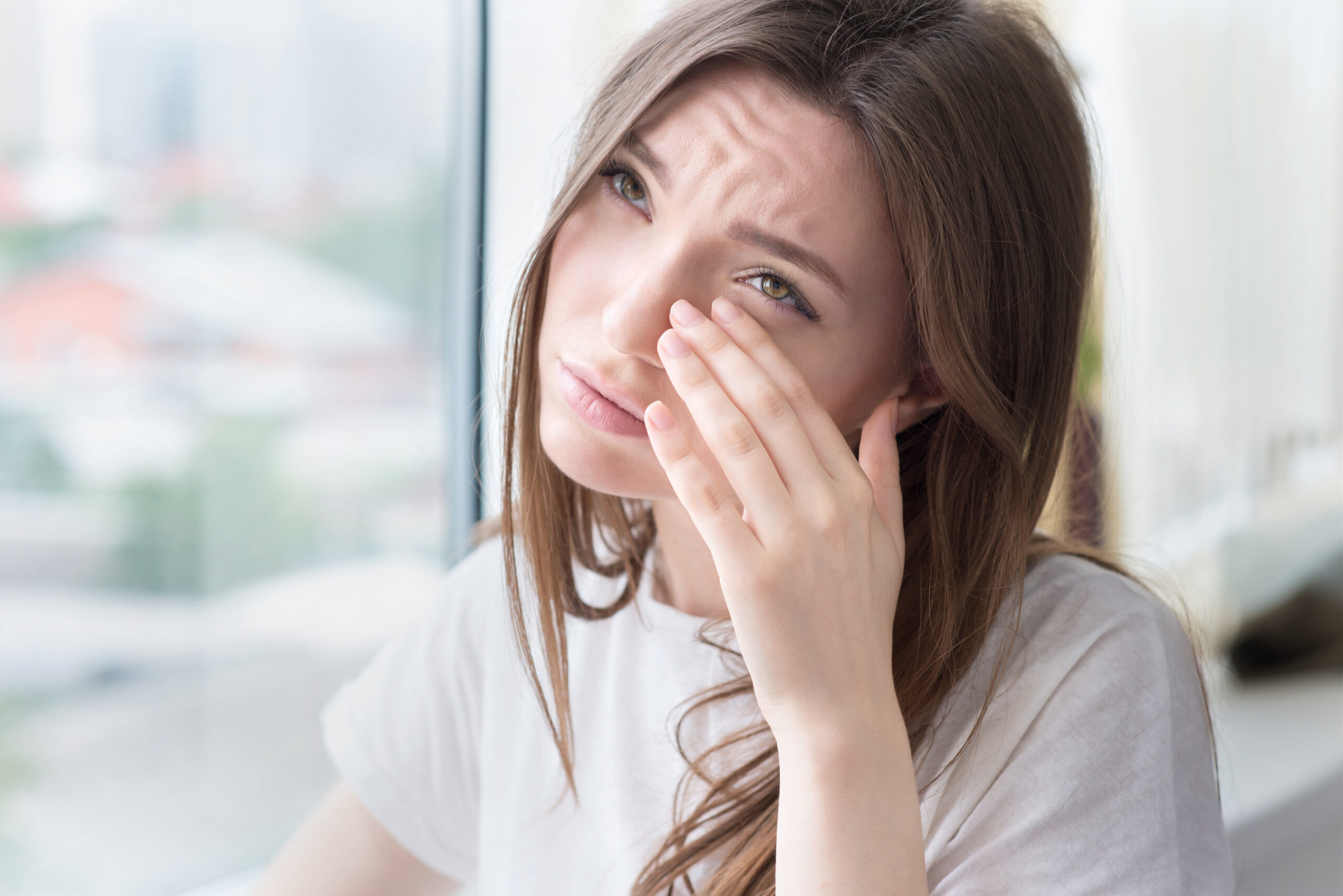 Young sad woman sits alone front of the window.