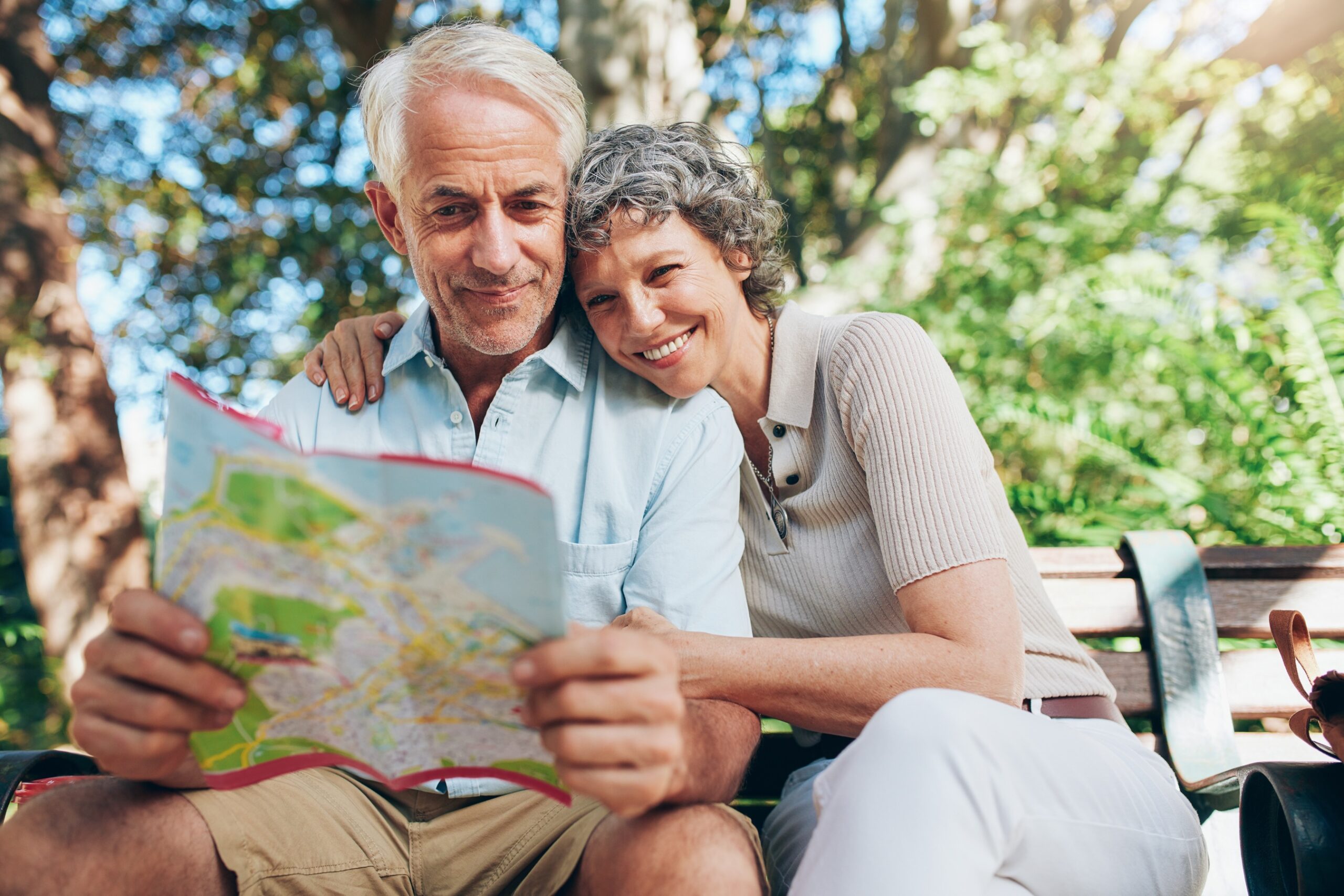 Happy senior couple relaxing on a park bench reading a city map.