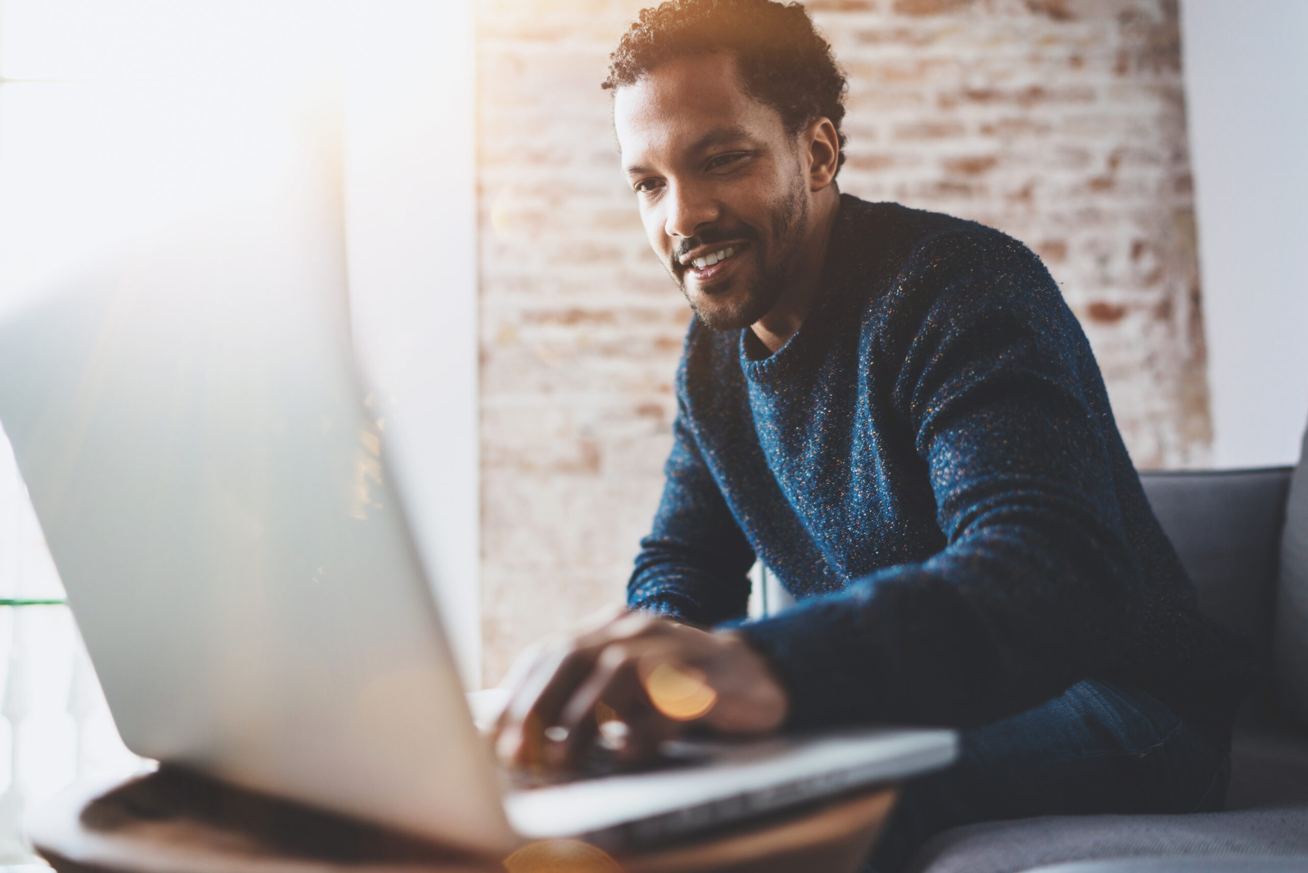 Man using computer and smiling while sitting on the sofa.