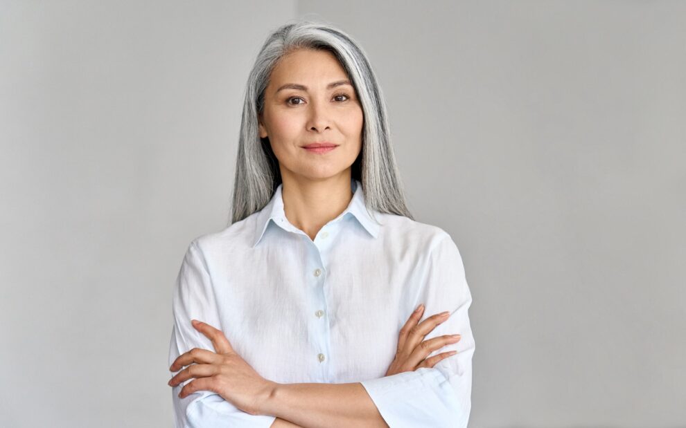 Woman standing arms crossed looking at camera at gray background